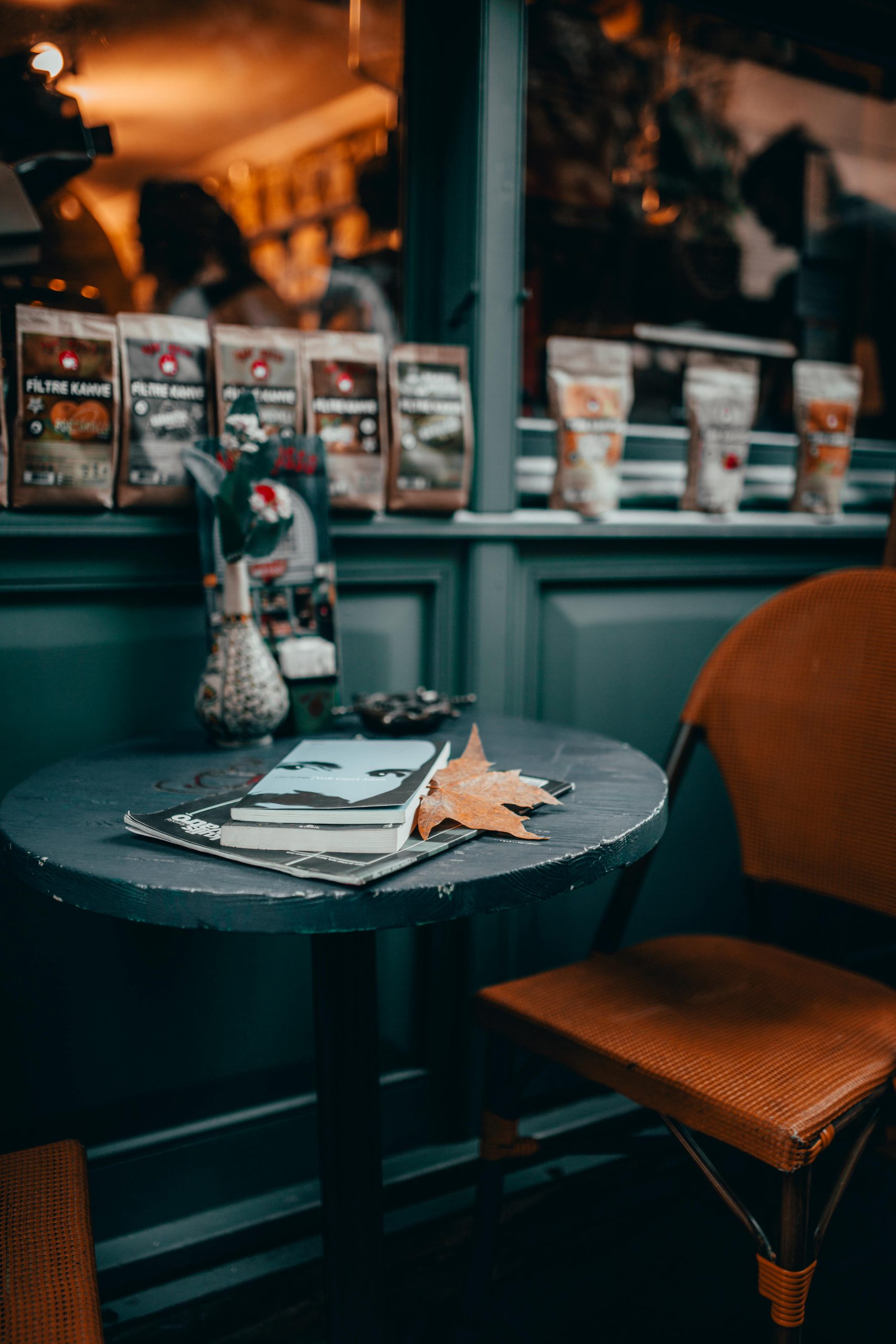 A cozy coffee shop table with books surrounded by autumn decor and seasonal leaves.